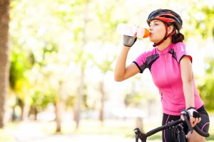 Young female cyclist drinking water while riding bicycle at park. 