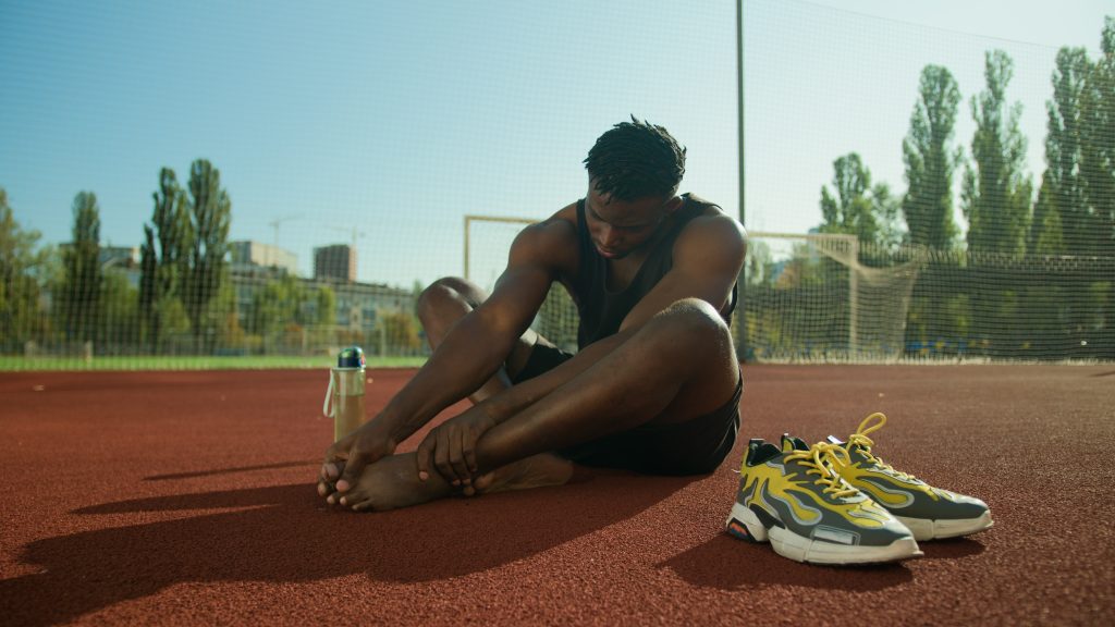 African American man feel ache painful leg pain injured foot after workout outdoors male sportsman footballer guy suffer injury bone finger callus health problem trauma accident on city sport ground. High quality 4k footage